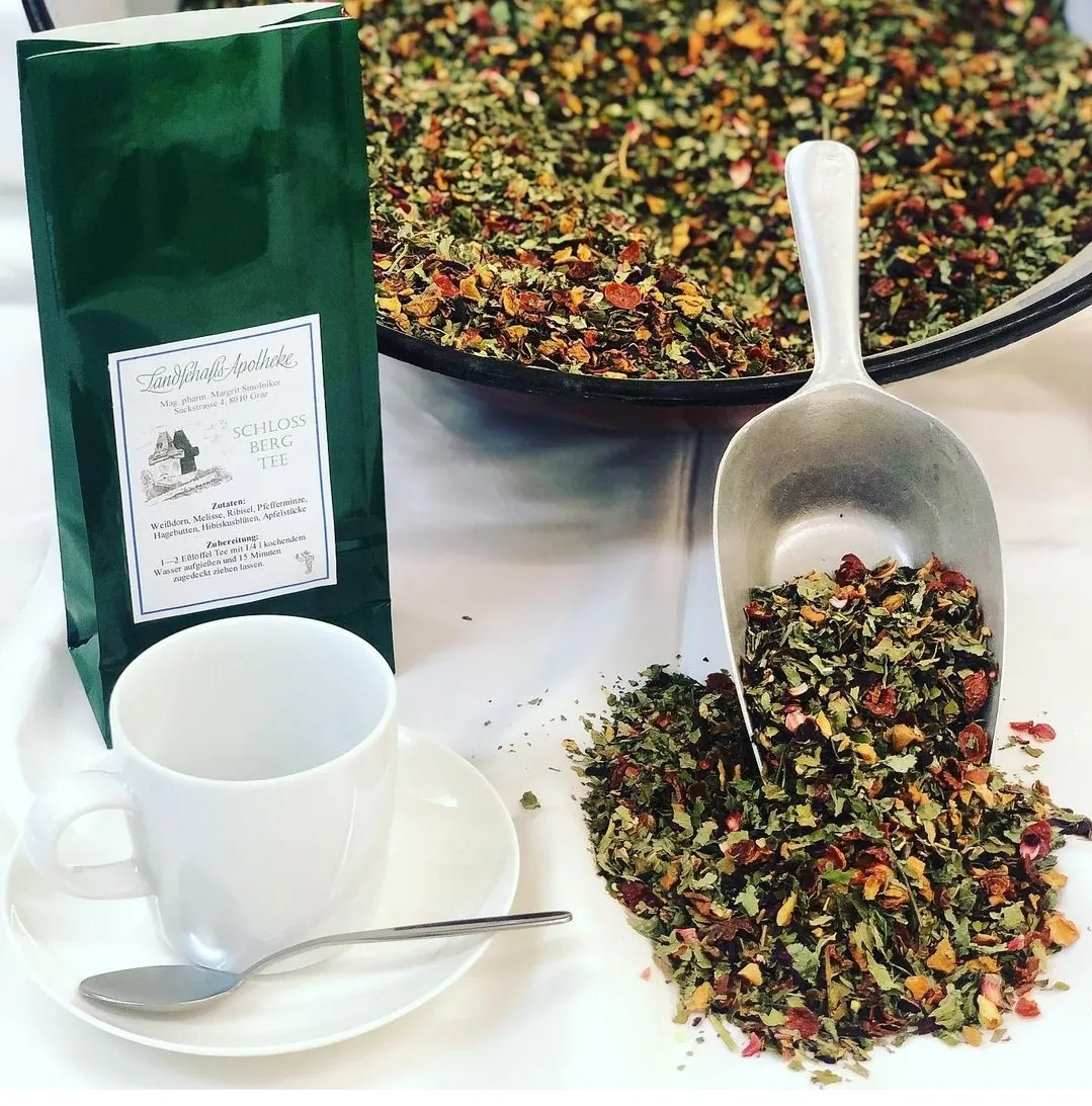 Teepackung der Landschafts-Apotheke neben losem Kräutertee, Schaufel und Teetasse
